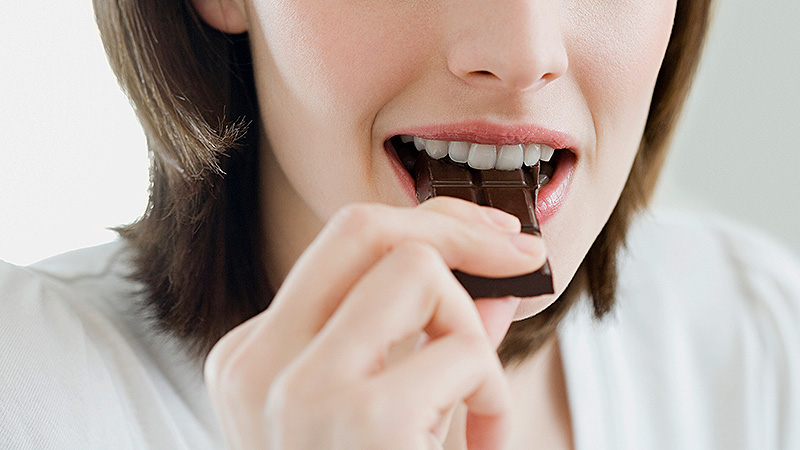 Девушка кусает плитку шоколада